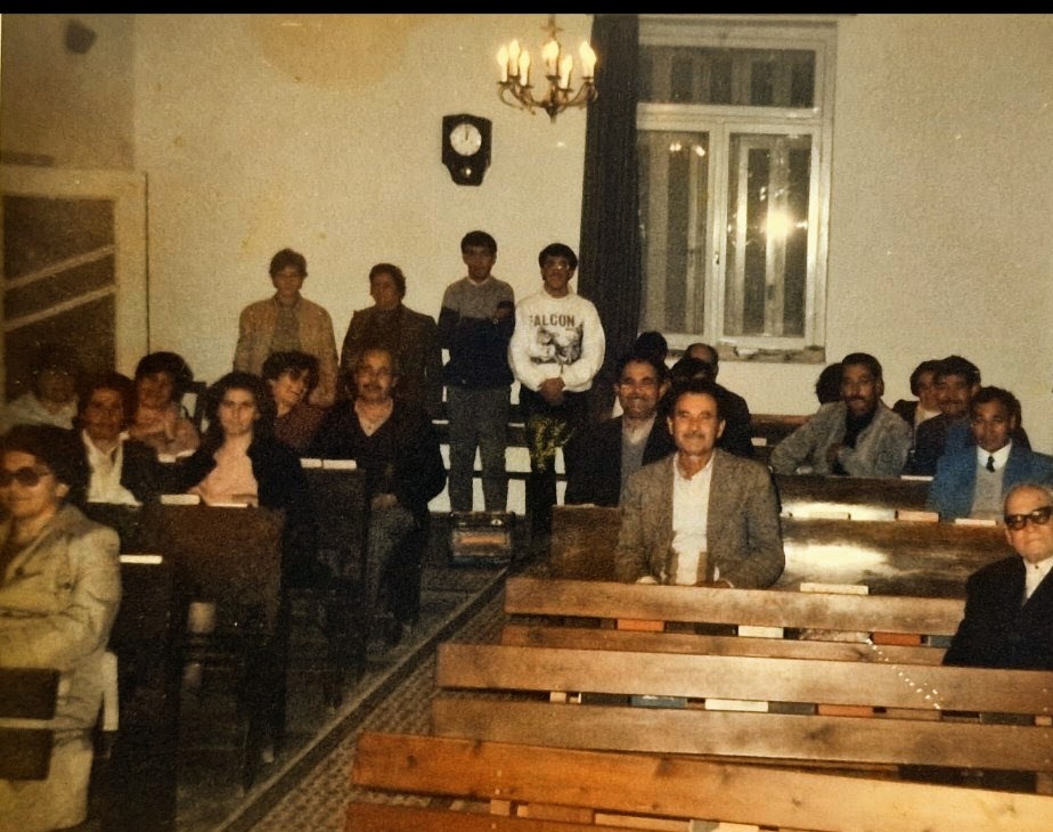 Church members seated and standing among wooden pews in the former worship hall.